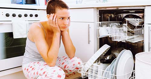 Image: a teenager looks anxiously at a broken dishwasher.