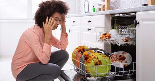 A woman looks frazzled over her dirty dishes in the dishwasher.